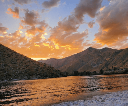 A serene lake at sunset, surrounded by mountains and colorful clouds reflecting on the water's surface.